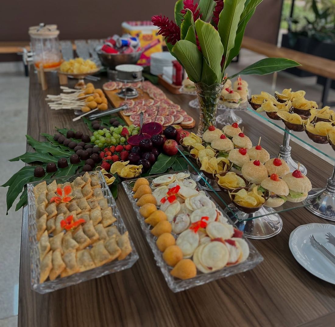 Happy hour com salgados, frutas e doces em mesa de madeira