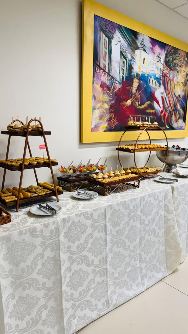 Mesa longa de coffee break com torres de salgados e doces