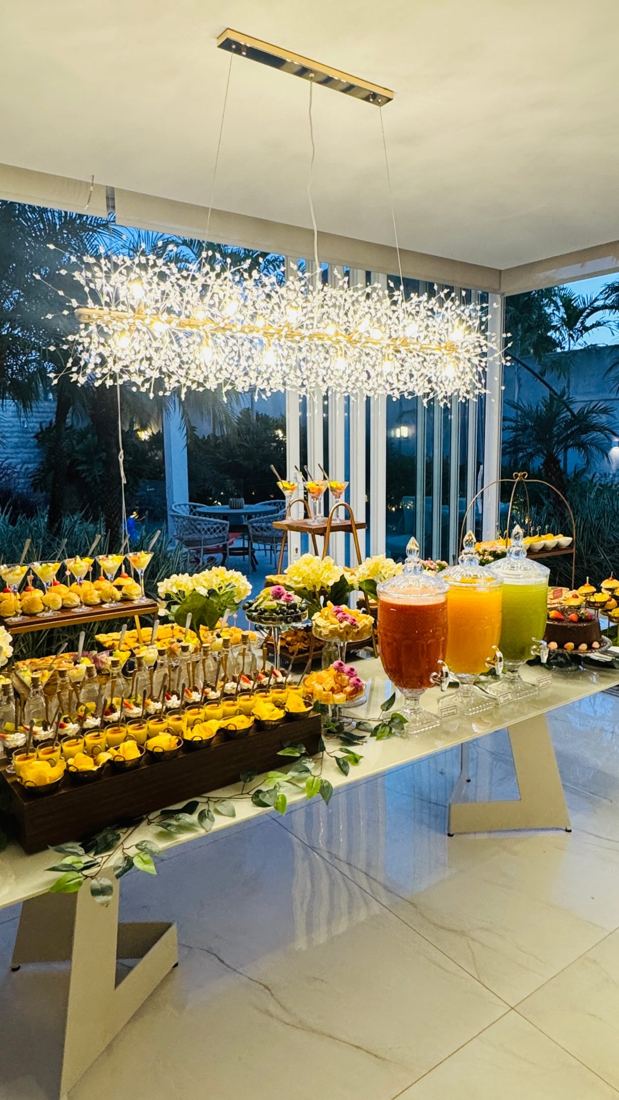 Mesa de brunch com bolos, frutas e sucos sob um lustre